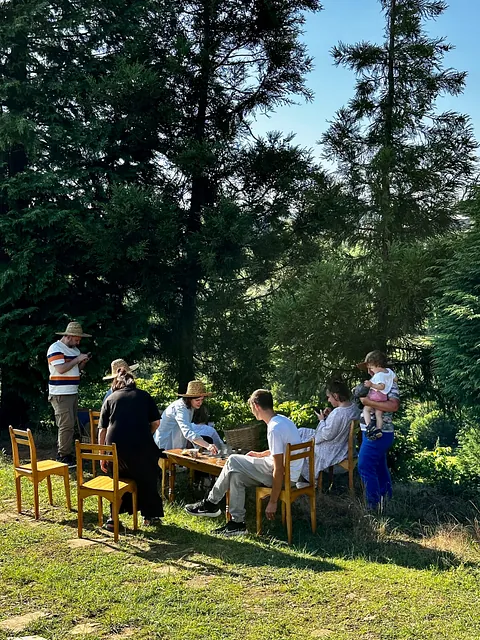 Im Wald sitzen Erwachsene auf Stühlen und an einem Tisch redend und spielend