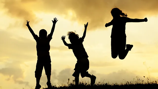 drei Silhouetten von springendn und jubelnden Kindern vor einem gelben Himmel 