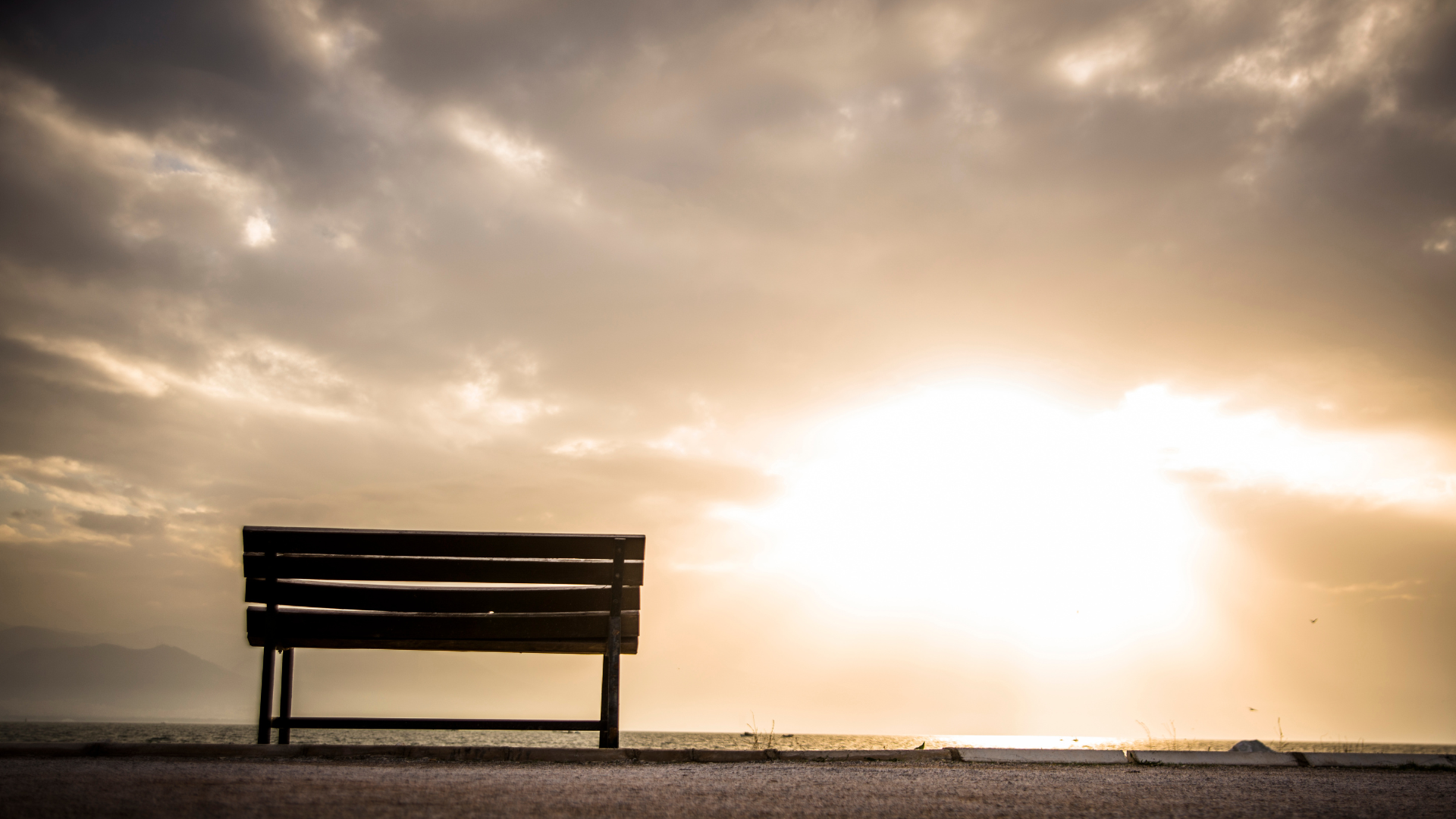 Sonne scheint, Wolkenhimmel, leere Bank mit Ausrichtung zur Sonne